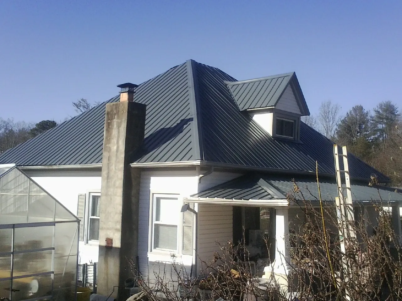 Dark blue standing seam metal roof on a white farmhouse with dormer — Slate & Tile Roof Repair by Roofing Brothers in New Franken