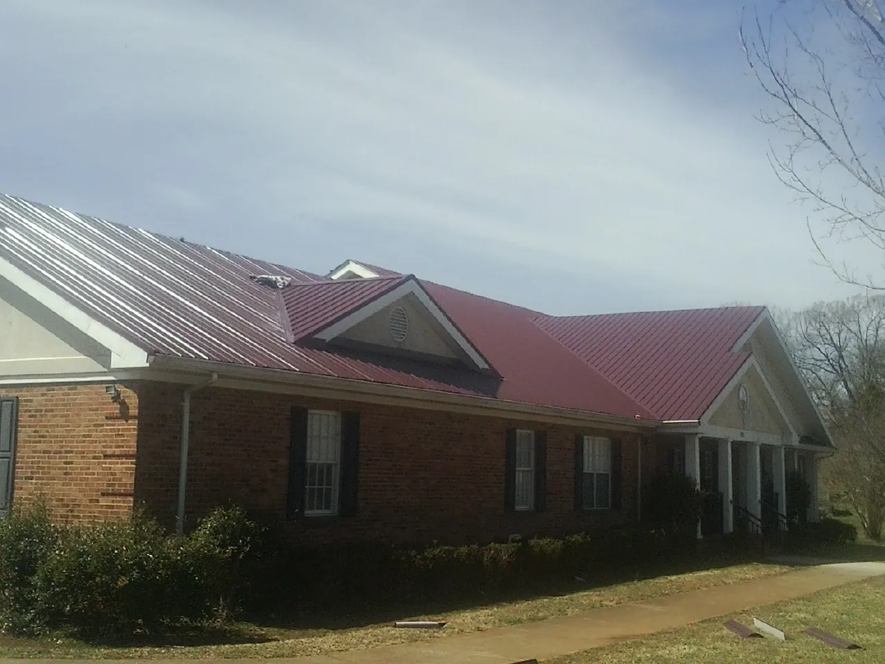 Red metal roof with gabled entries on a long brick building, from a Hail Damage Roof Repair job in New Franken