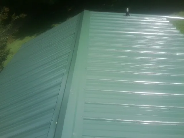 New green metal panels meeting at the ridge of a roof — Flat Roof Repair work by our crew in New Franken