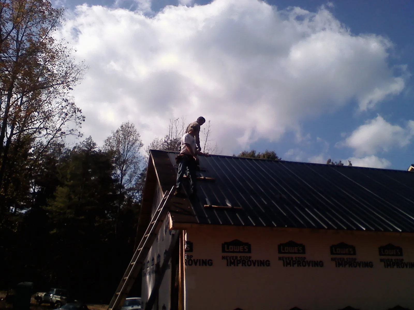 Roofer fastening dark metal panels high against a cloudy sky, from a Roof Inspection job in New Franken