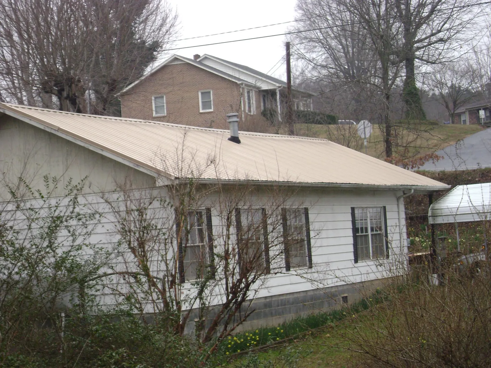 Tan metal roof on a white sided house set into a hillside — Commercial Roofing by Roofing Brothers in New Franken