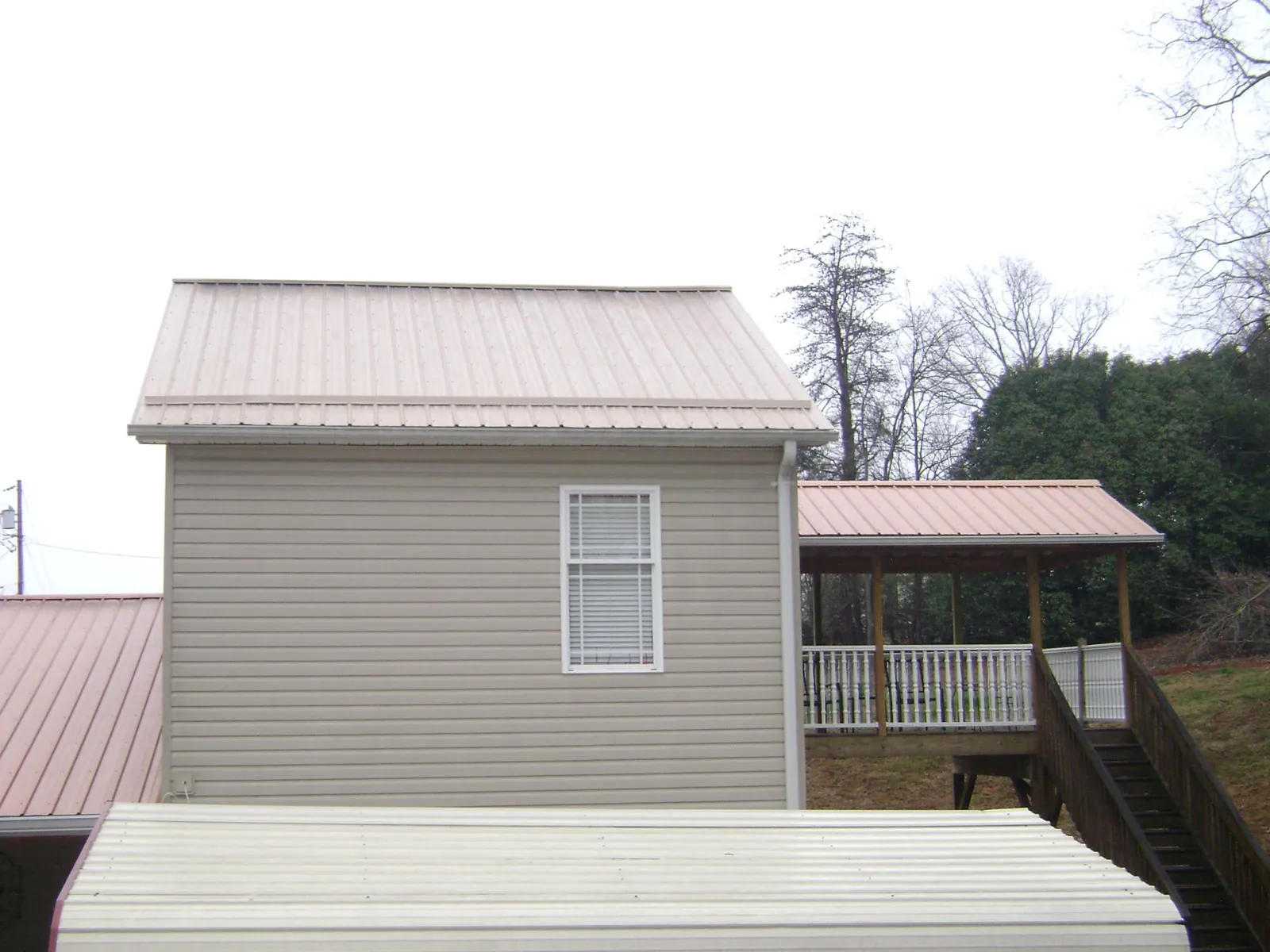 Tan metal roofs on a two story addition and attached porch, from a Roof Replacement job in New Franken
